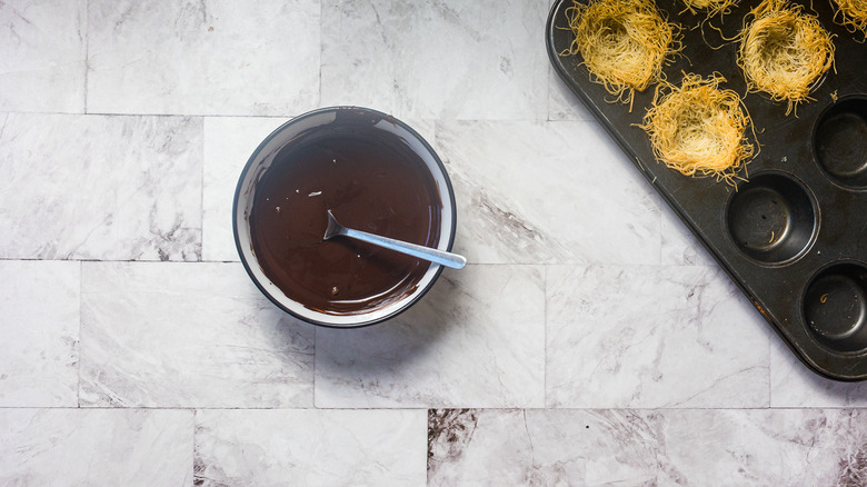 Melted chocolate in bowl besides noodles