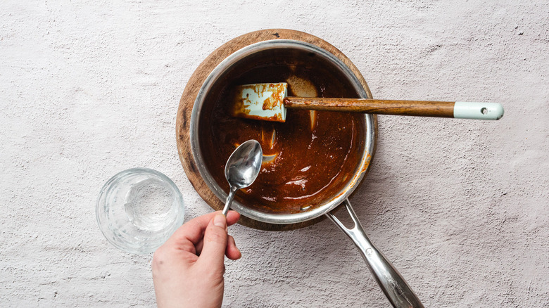 Adding water with a spoon to glaze in saucepan with spatula