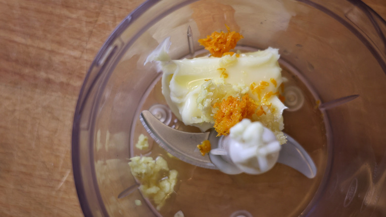 food processor with butter, orange zest, ginger, and garlic in it
