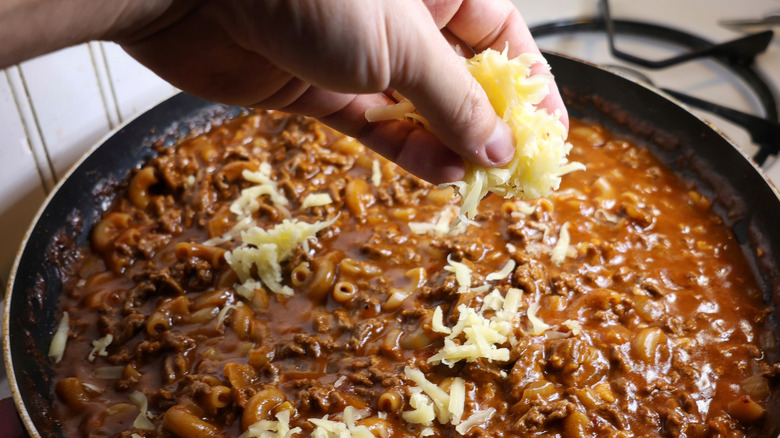 hand sprinkling shredded cheese into skillet of Hamburger Helper