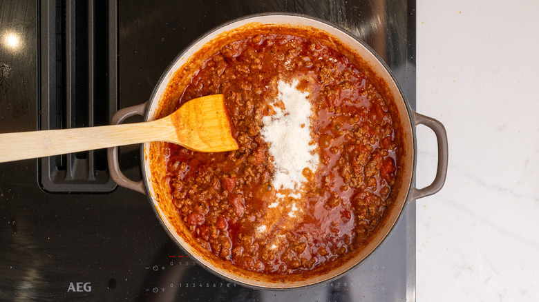 masa harina added to a pan of chili on stovetop with spatula inside