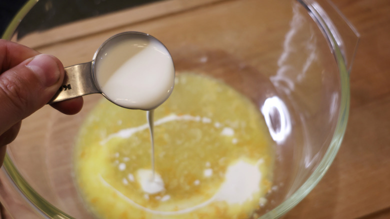cream pouring from measuring spoon into mixing bowl of melted butter