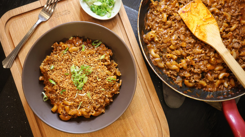 overhead shot of garnished bowl of Hamburger Helper next to skillet of Hamburger Helper