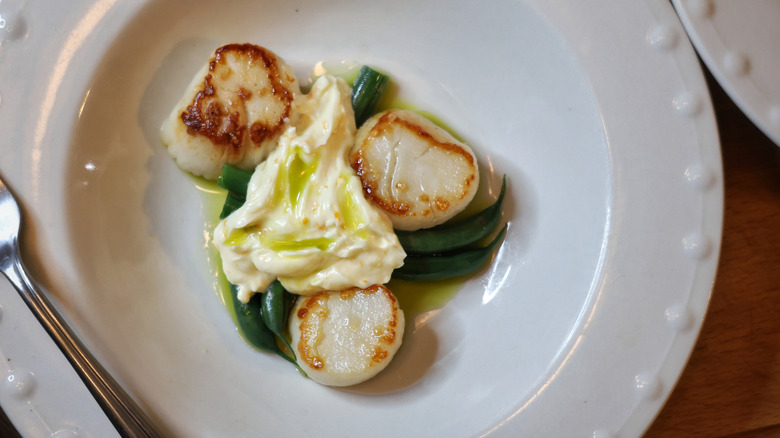 overhead shot of scallops and green beans plated in a shallow white bowl with basil oil and orange ginger compound butter
