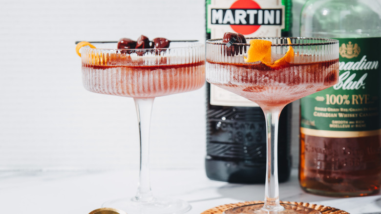 Side view of two frozen Manhattan cocktails with two liquor bottles.