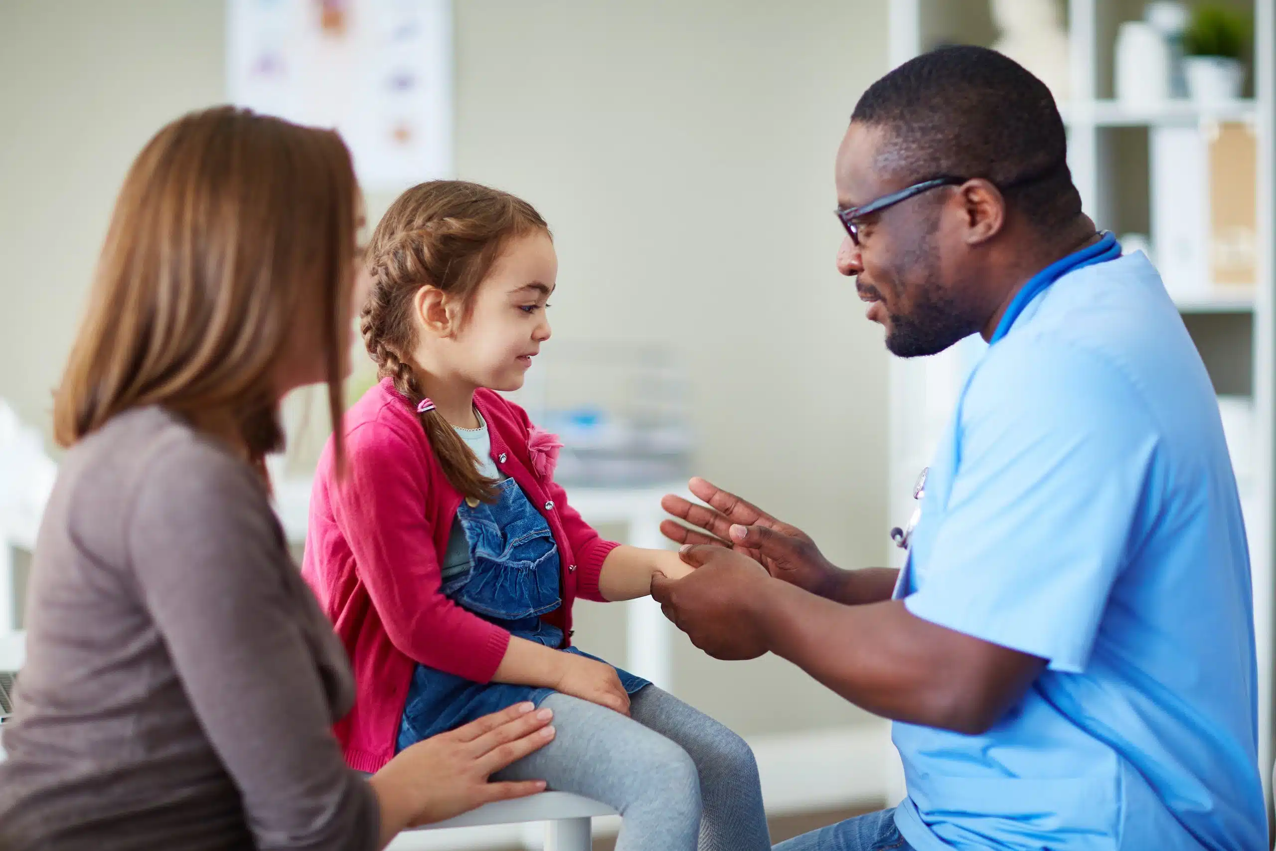 Physician assistant helping a young girl with her mother sitting by.