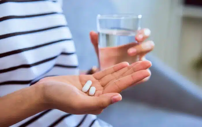 Woman holding white pill on hand and a glass of water