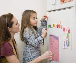 Woman and child having fun with magnetic letters on a fridge