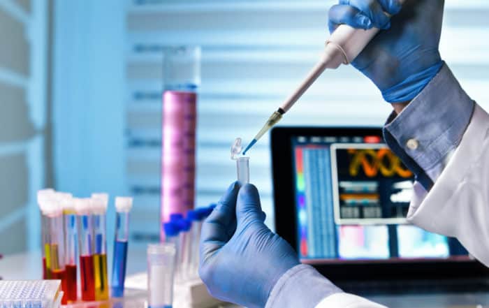 scientist holding tube and working with laptop at genetic lab / hands of engineer genetic working in laboratory