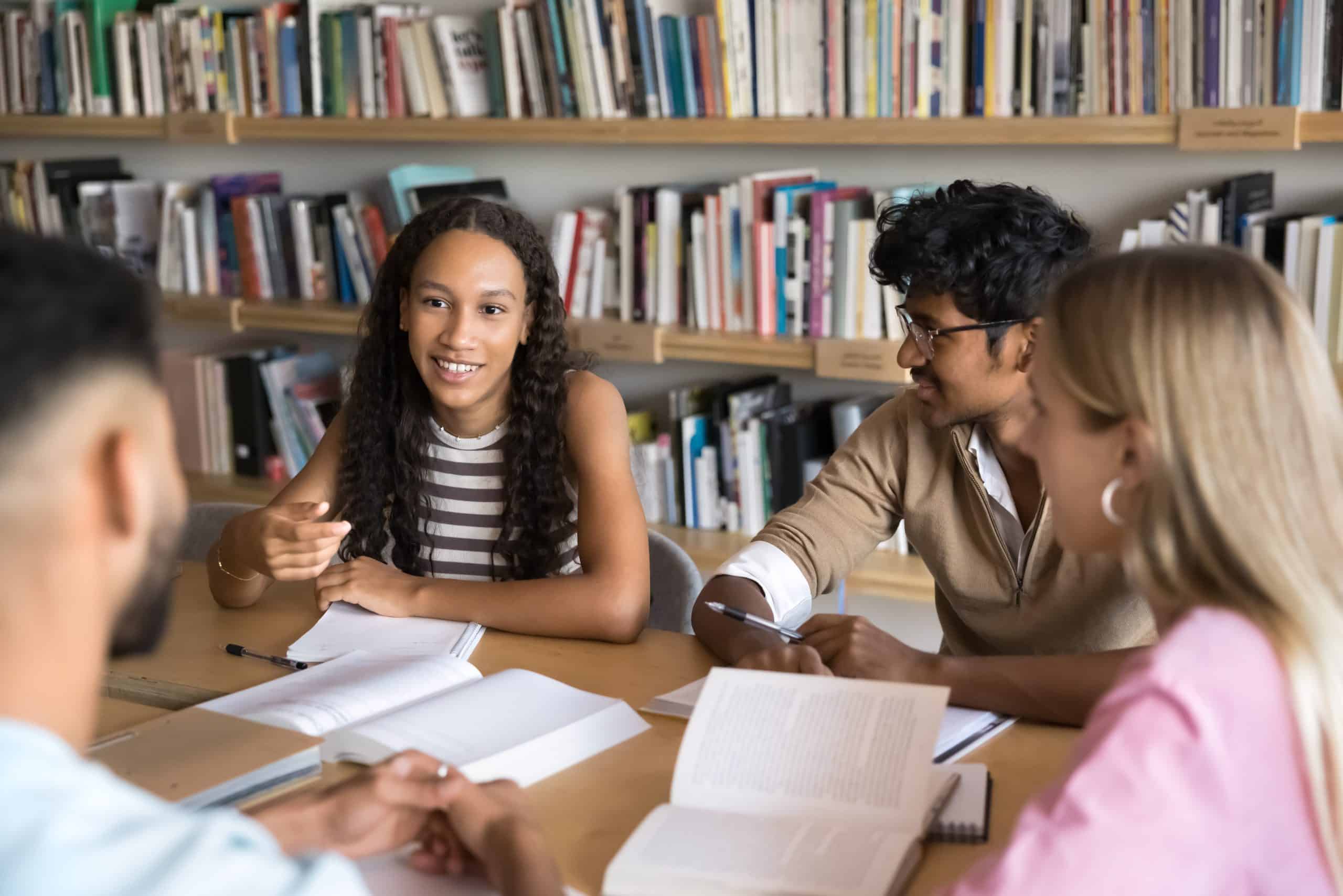 Group of multinational high school or university students engaged in exam preparation, sharing ideas, testing each other, studying together met in library, focus on African girl explain point of view