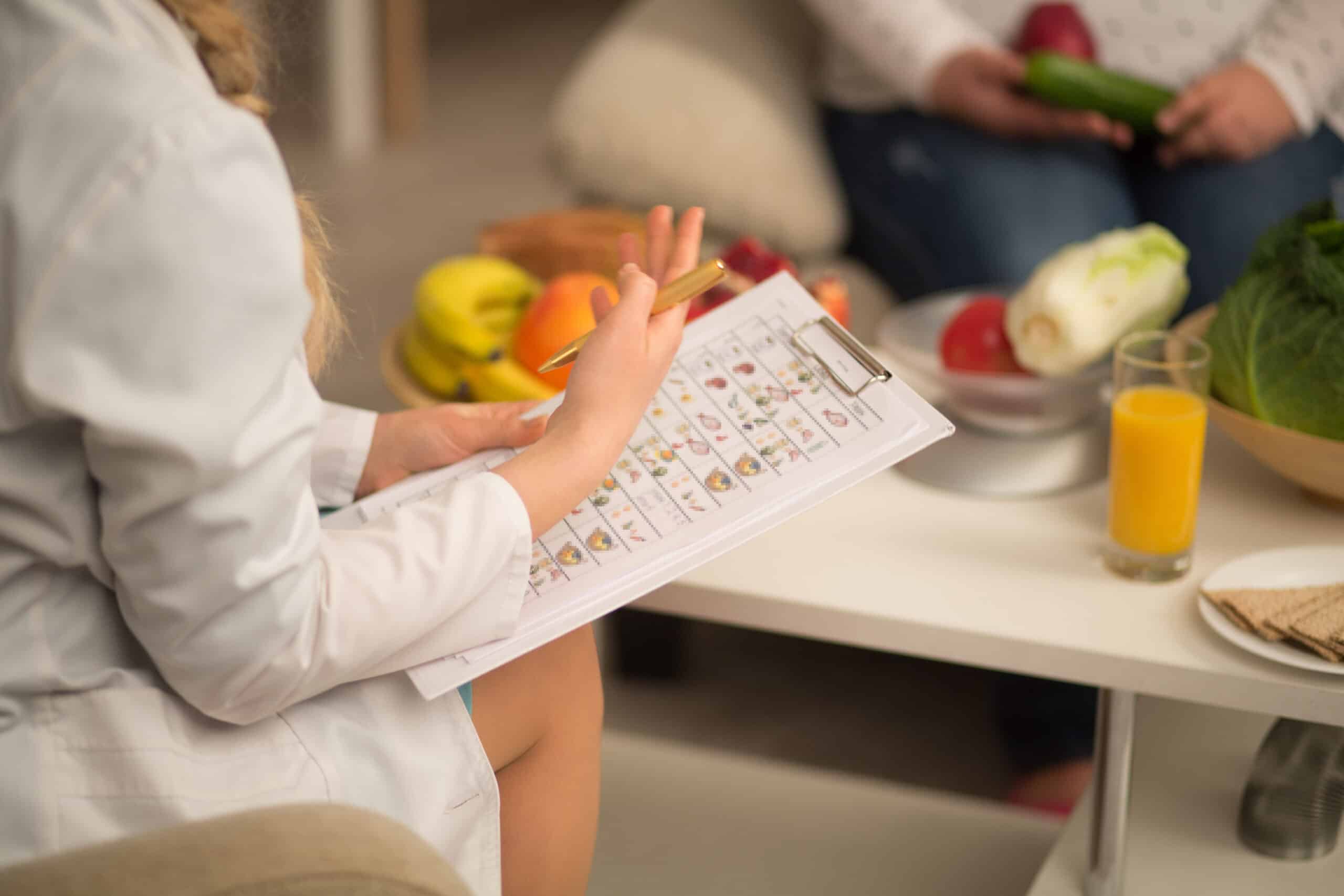 Close up image of dietitian in white gown. holding die plan for patient, having fruits and vegetables on the white table