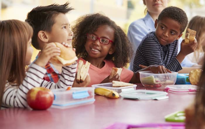 Young school kids eating lunch talking at a table together
