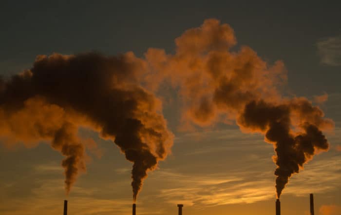 Smoke or gas billowing from industrial smokestack chimneys, lit orange and red by the morning sunrise.