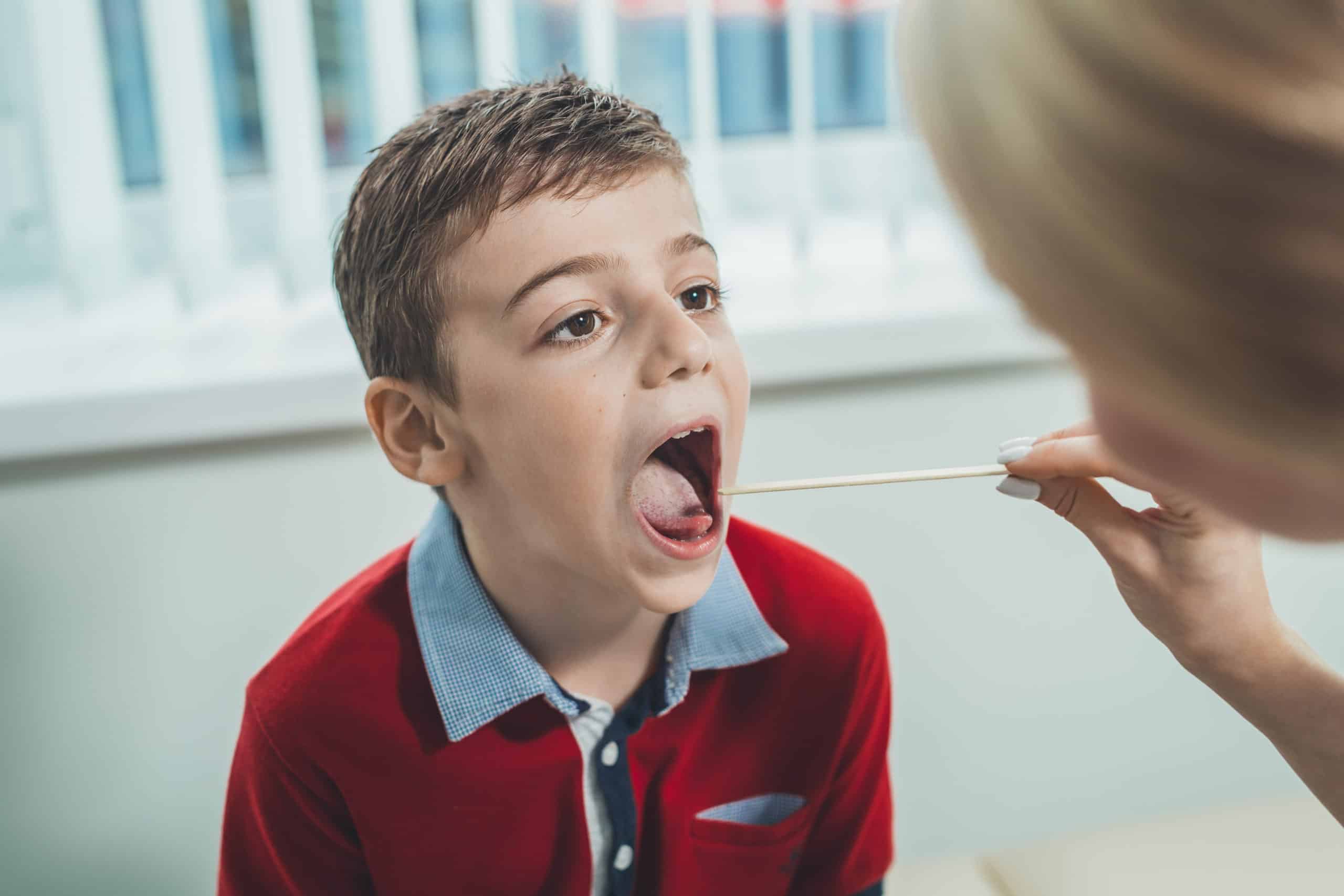 Boy has strep throat. Children's ENT doctor examines boy's throat. Children's diseases, medical examination.