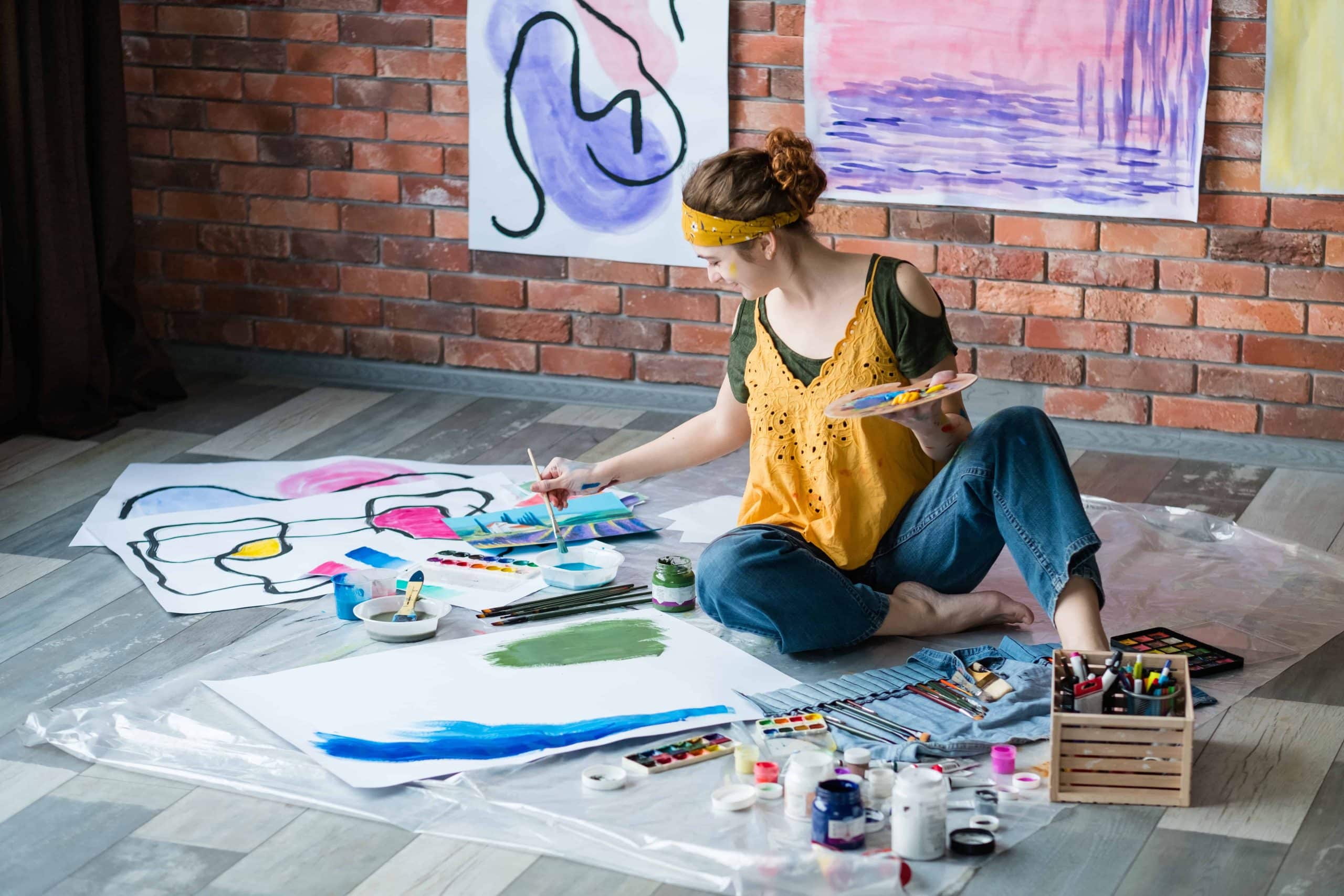 Modern art school. Female artist sitting on floor, painting abstract artworks. Creative workplace.