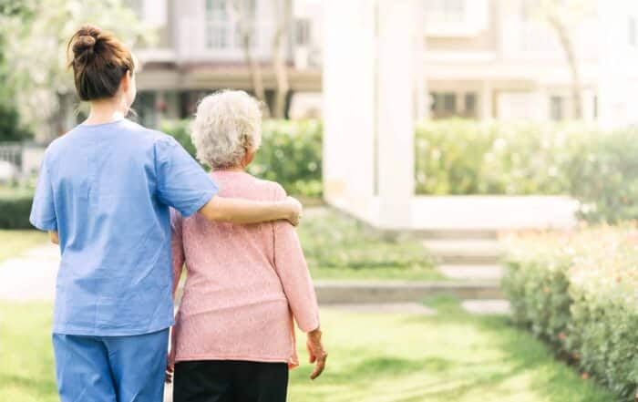 Back view of nurse caregiver support walking with elderly woman outdoor