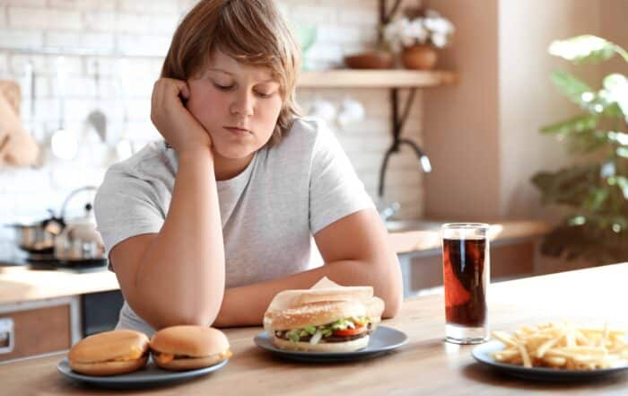Overweight boy at table with fast food in kitchen