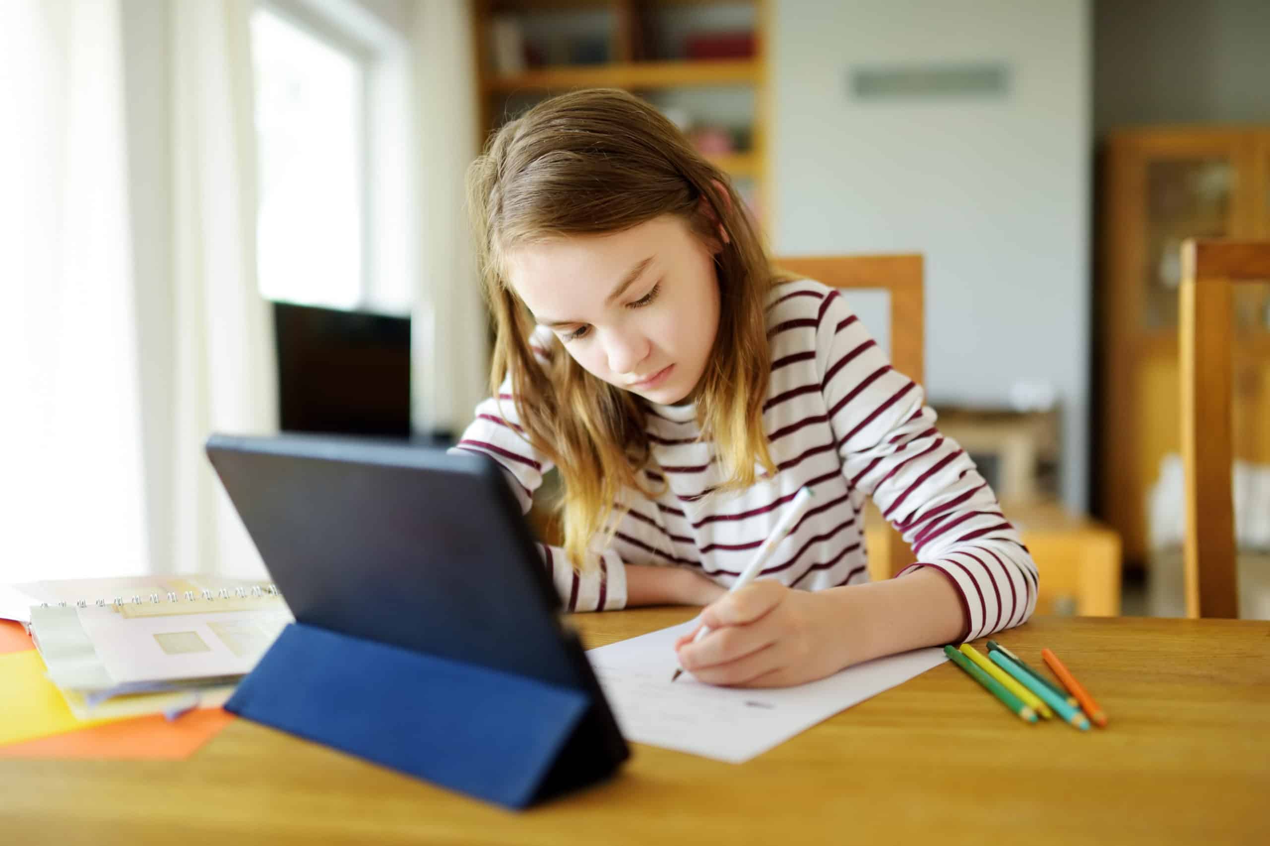 Preteen schoolgirl doing her homework with digital tablet at home. Child using gadgets to study. Education and distance learning for kids. Homeschooling during quarantine. Stay at home entertainment.