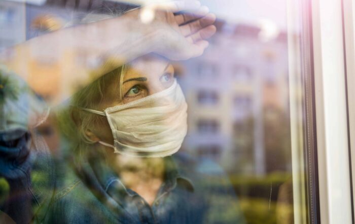 Close-up of a woman wearing a white mask, looking outside through a window