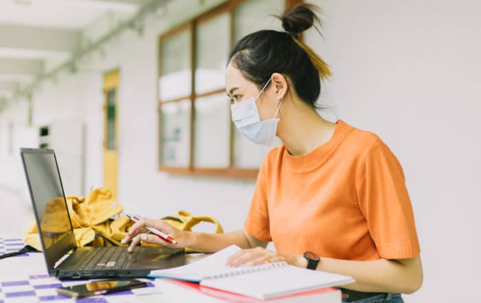 Asian teen woman working alone wearing face mask in university.