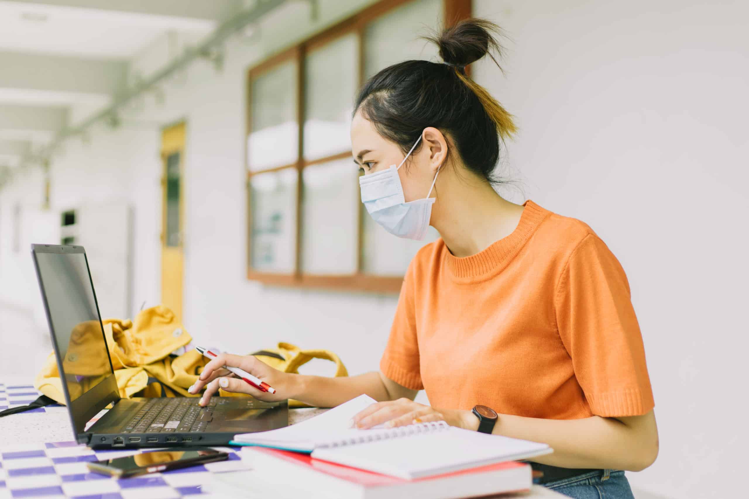 Asian teen woman working alone wearing face mask in university.