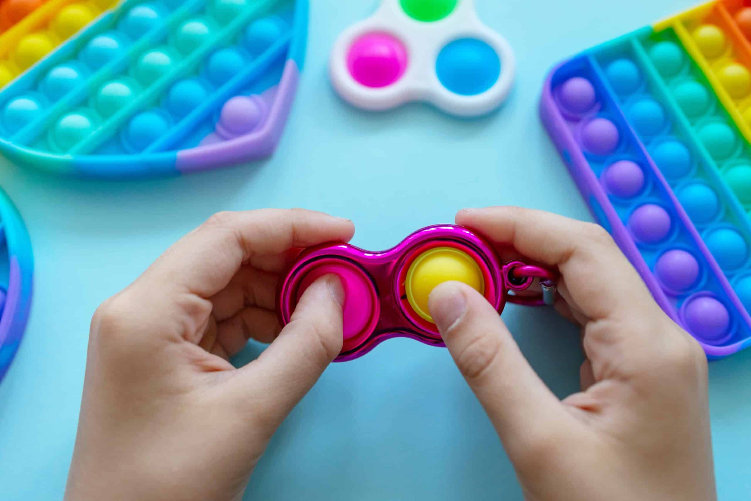 Colorful trendy antistress sensory toy fidget push pop it and simple dimple in kid's hands on blue background