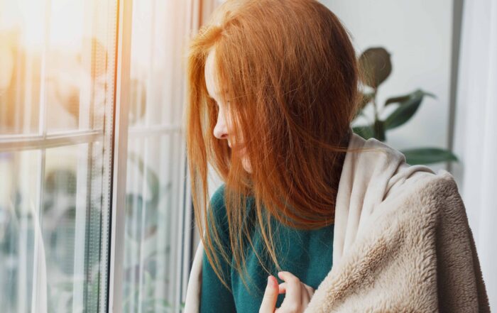 Close-up of a woman with ginger hair, looking outside through a window