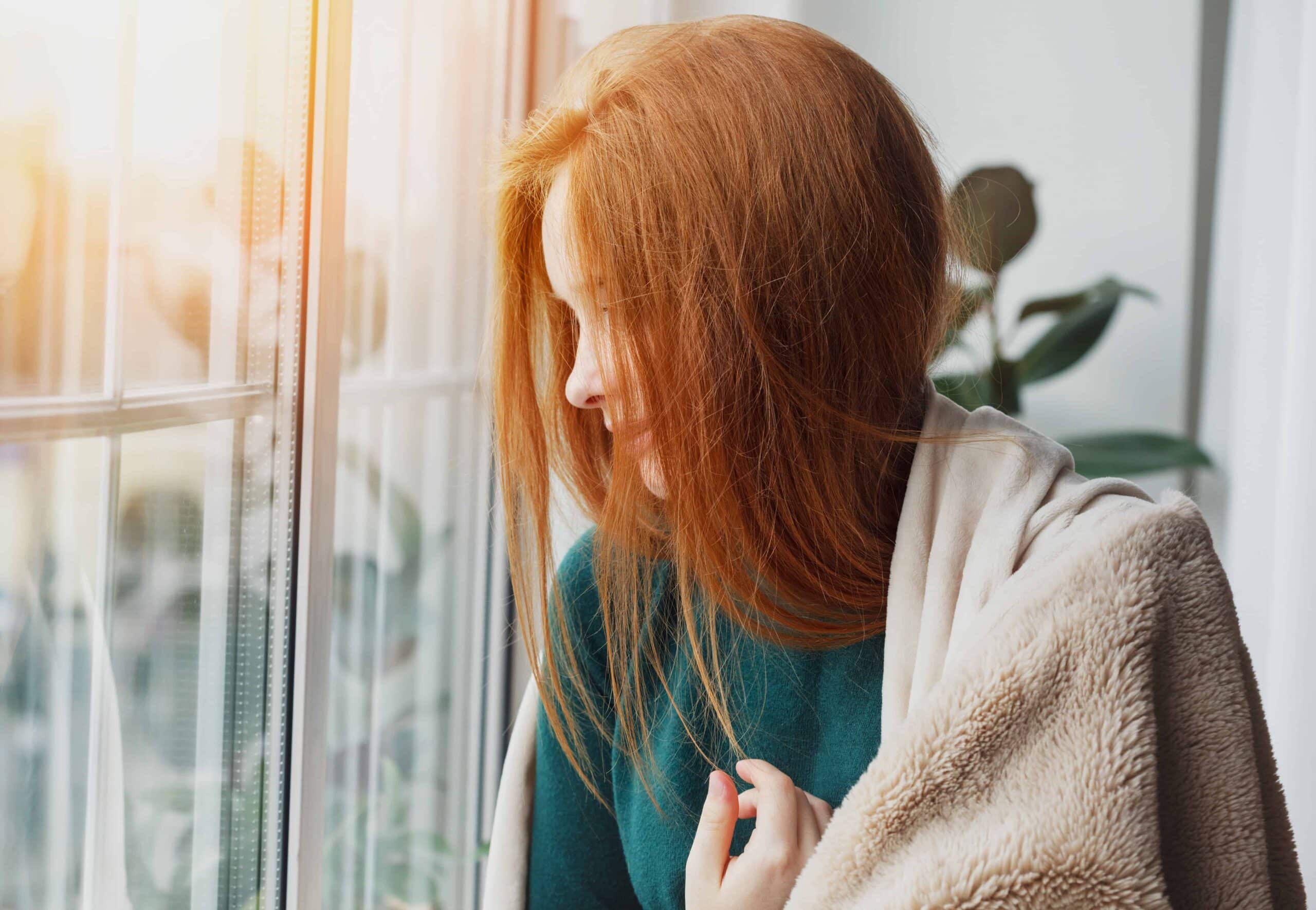 Close-up of a woman with ginger hair, looking outside through a window