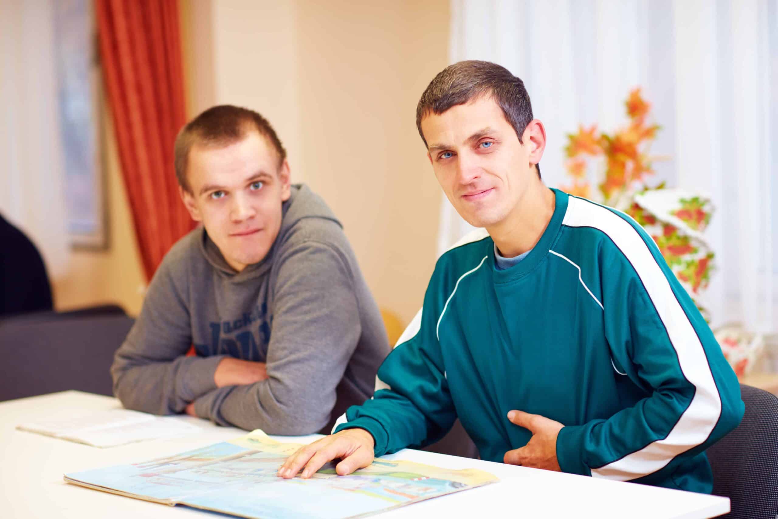cheerful adult men with disability sitting at the desk in rehabilitation center
