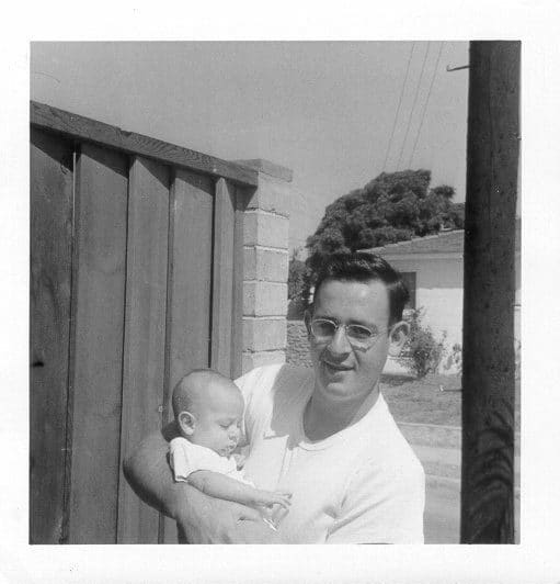 Man holding a baby outside in front of a house