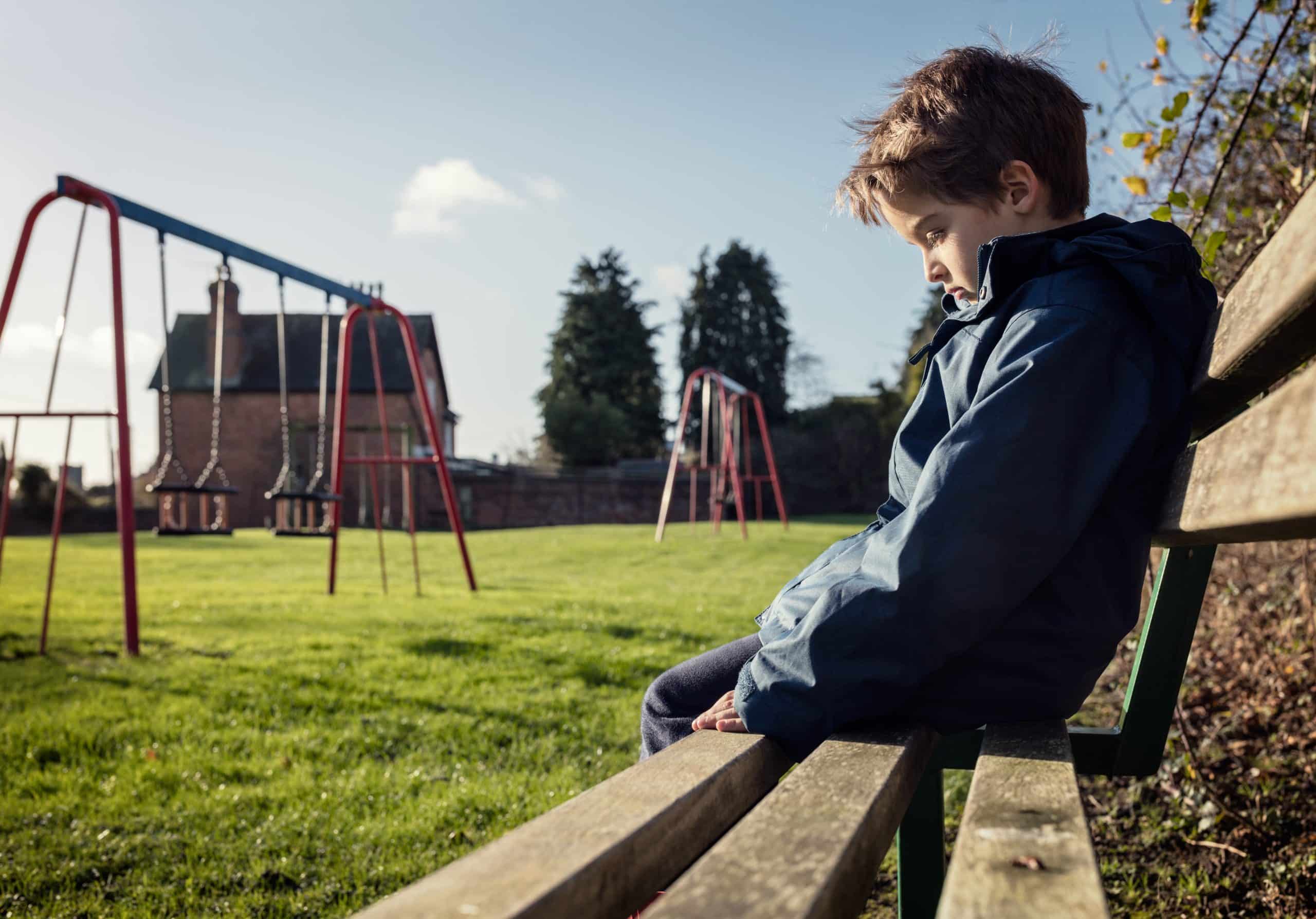 Upset child sitting alone on a playground bench