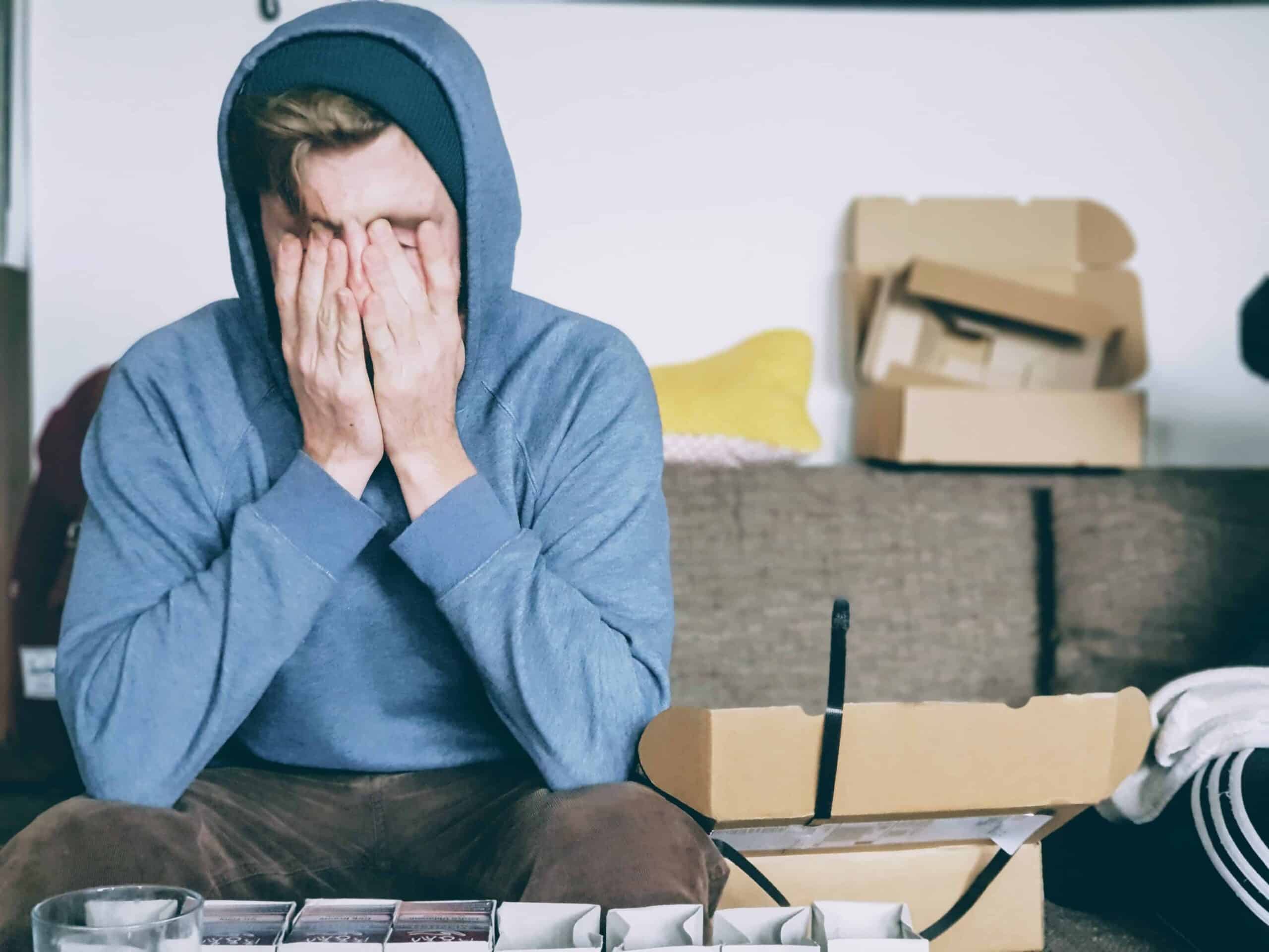 Man looking distressed while sitting on a sofa surrounded by boxes