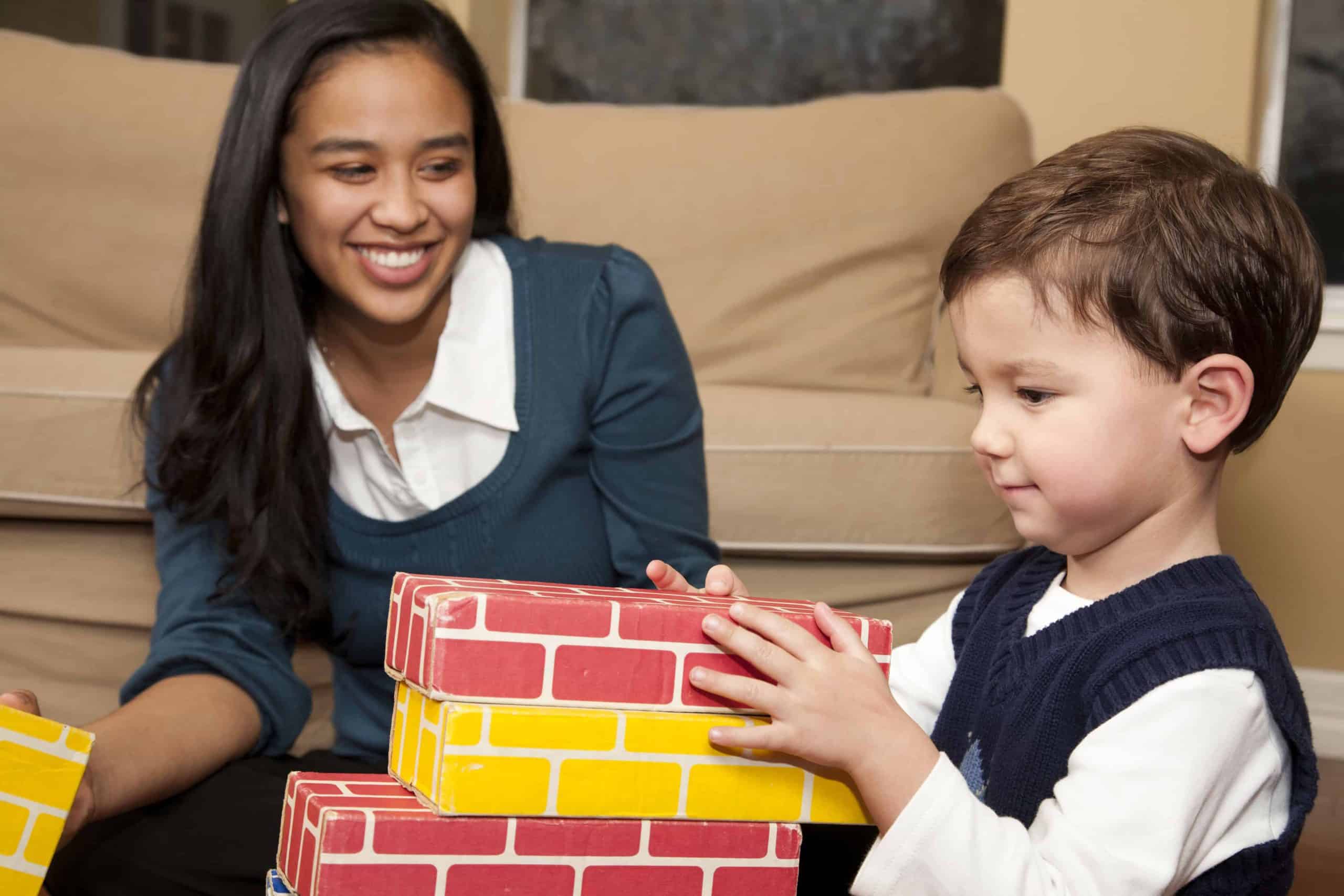 Young kid enjoying playtime with colorful bricks, mom smiling at him