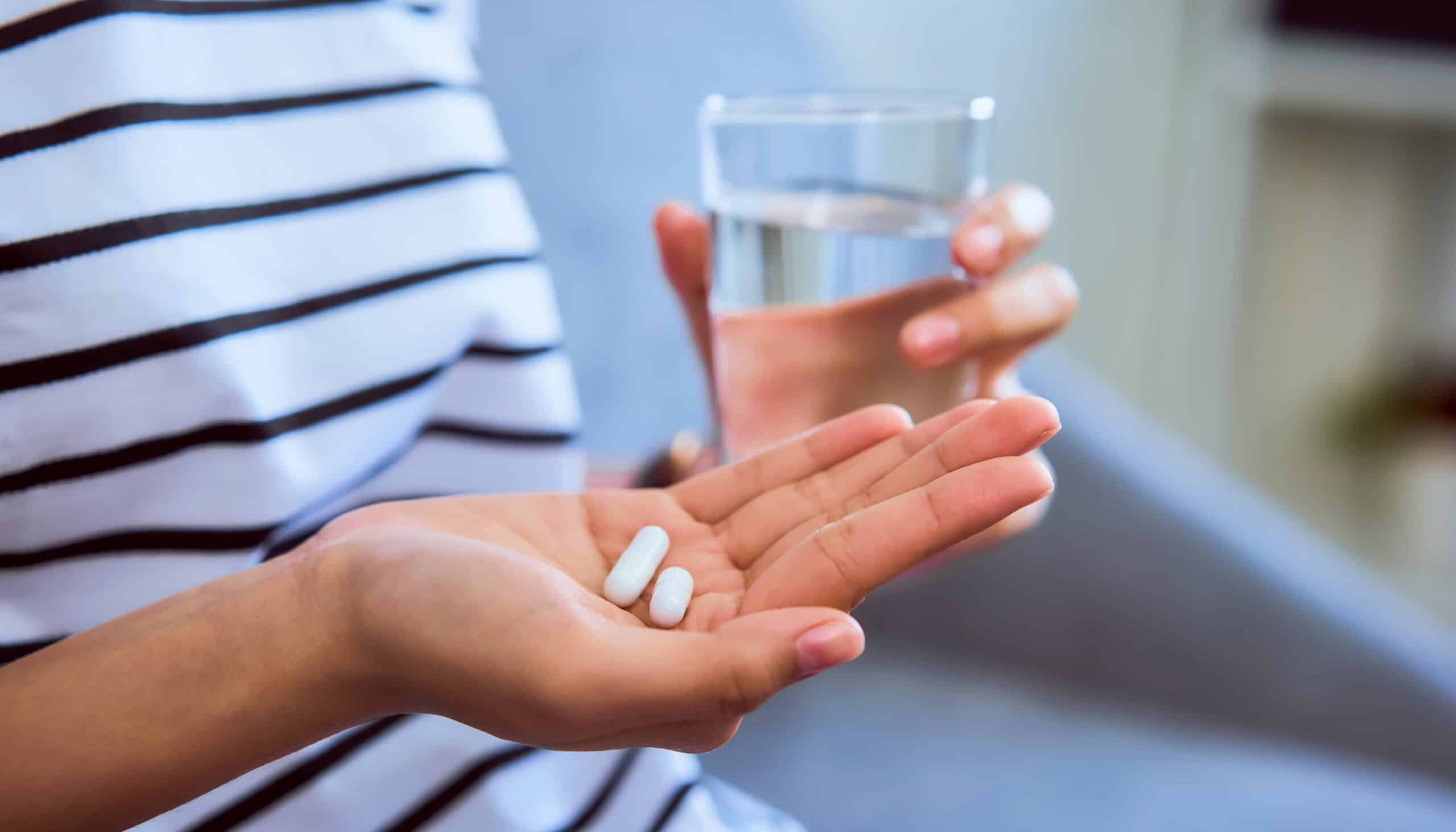 Woman holding white pill on hand and a glass of water