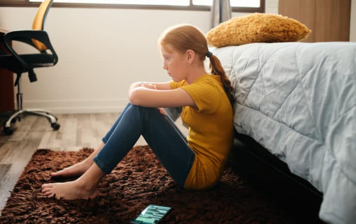 Upset young girl sitting on the floor of her bedroom, feeling down
