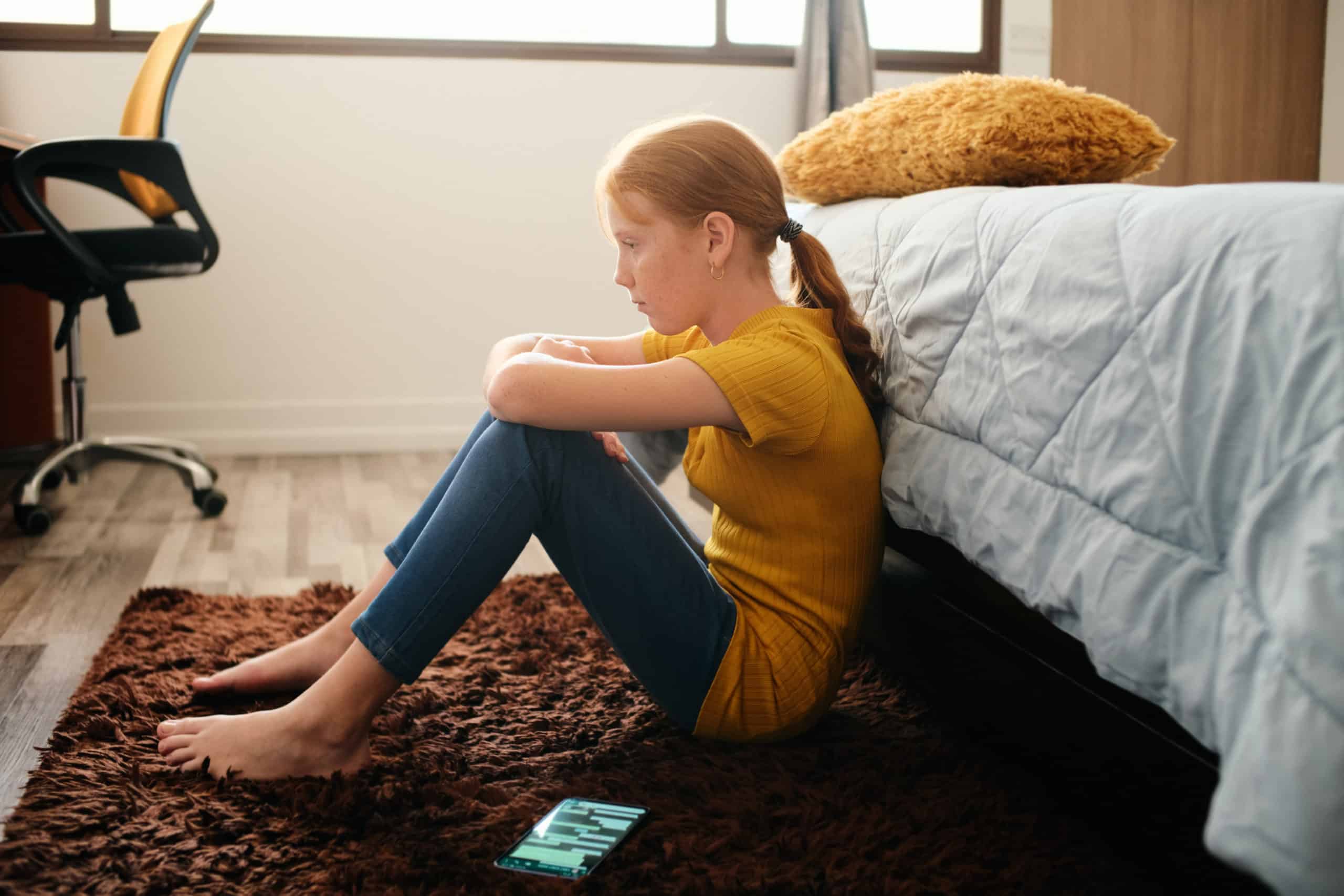 Young girl with a sad expression sitting on the floor in her room