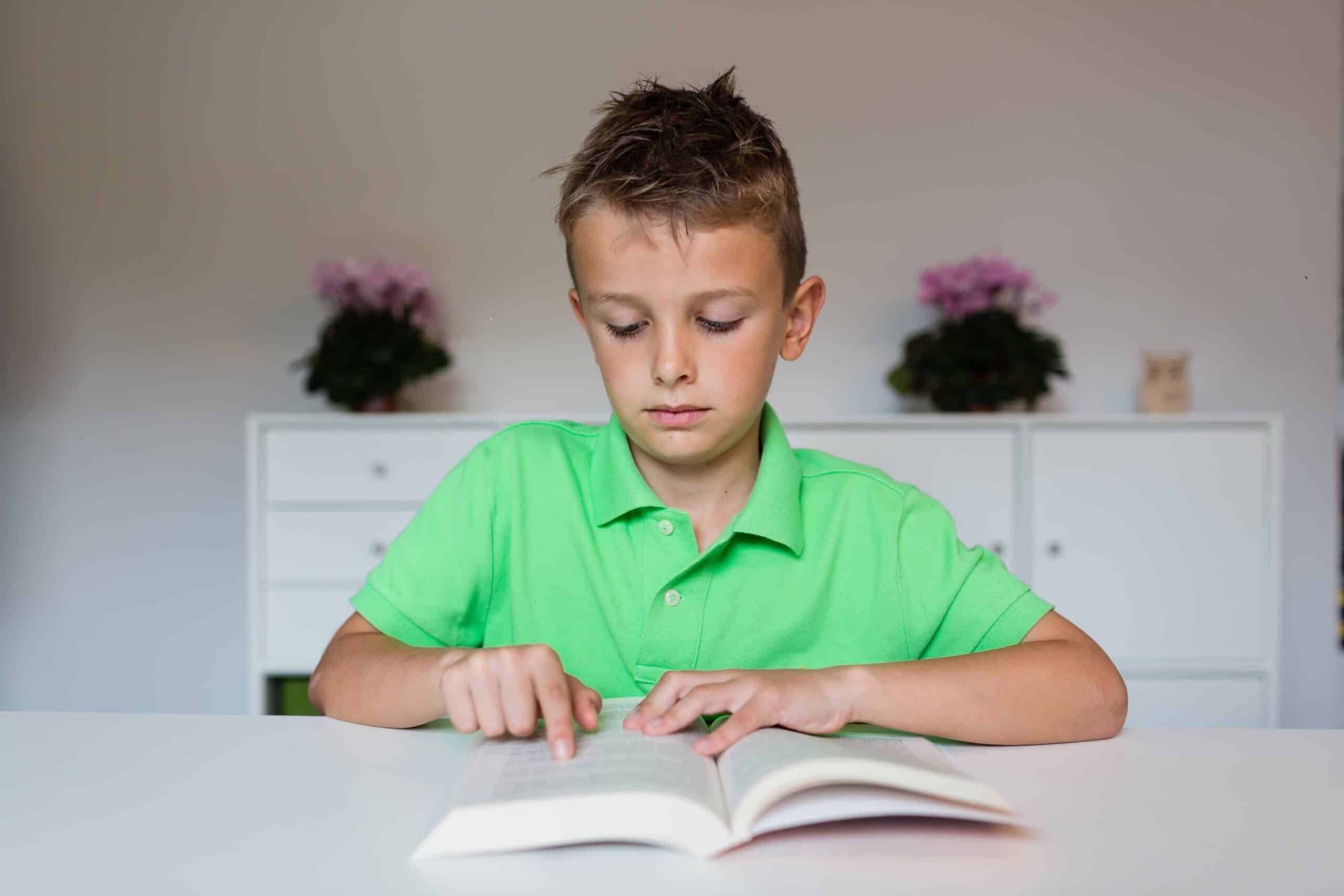 Young boy in green polo shirt having challenges reading a text in a school book.