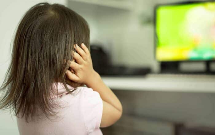 Child covering her ears while looking at a TV screen in the background