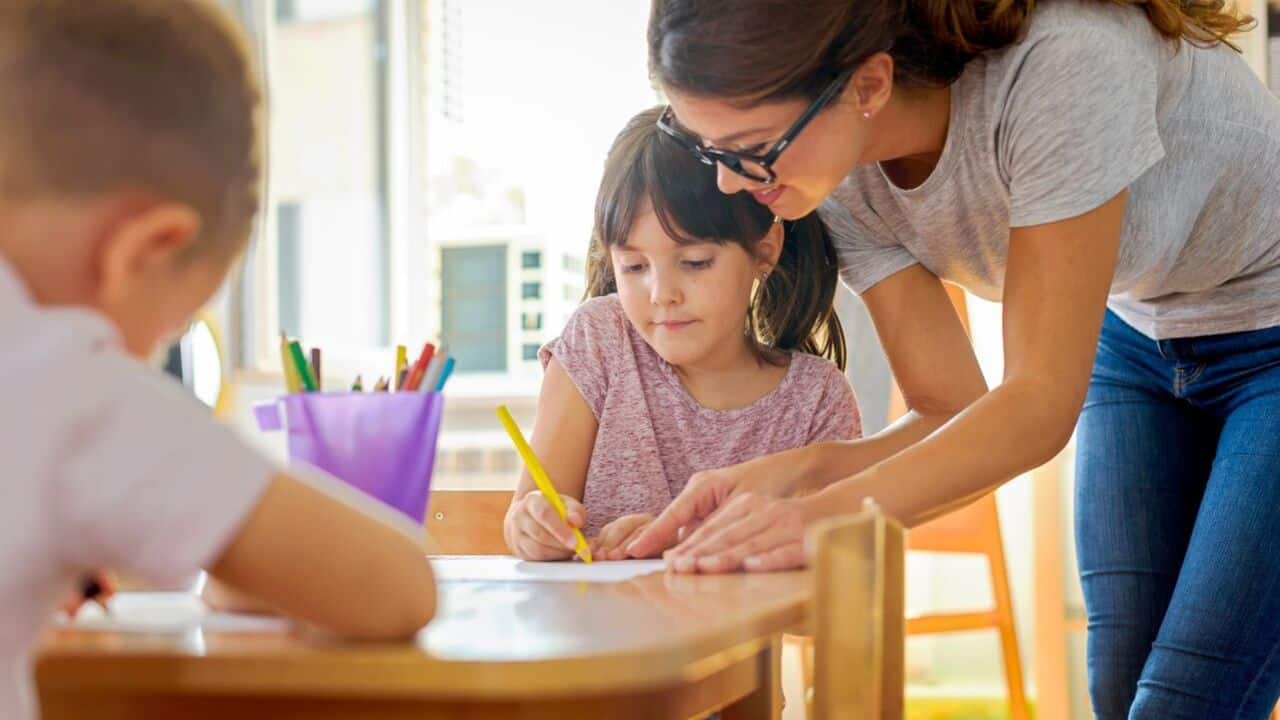 Children working on assignments in class with teacher assistance