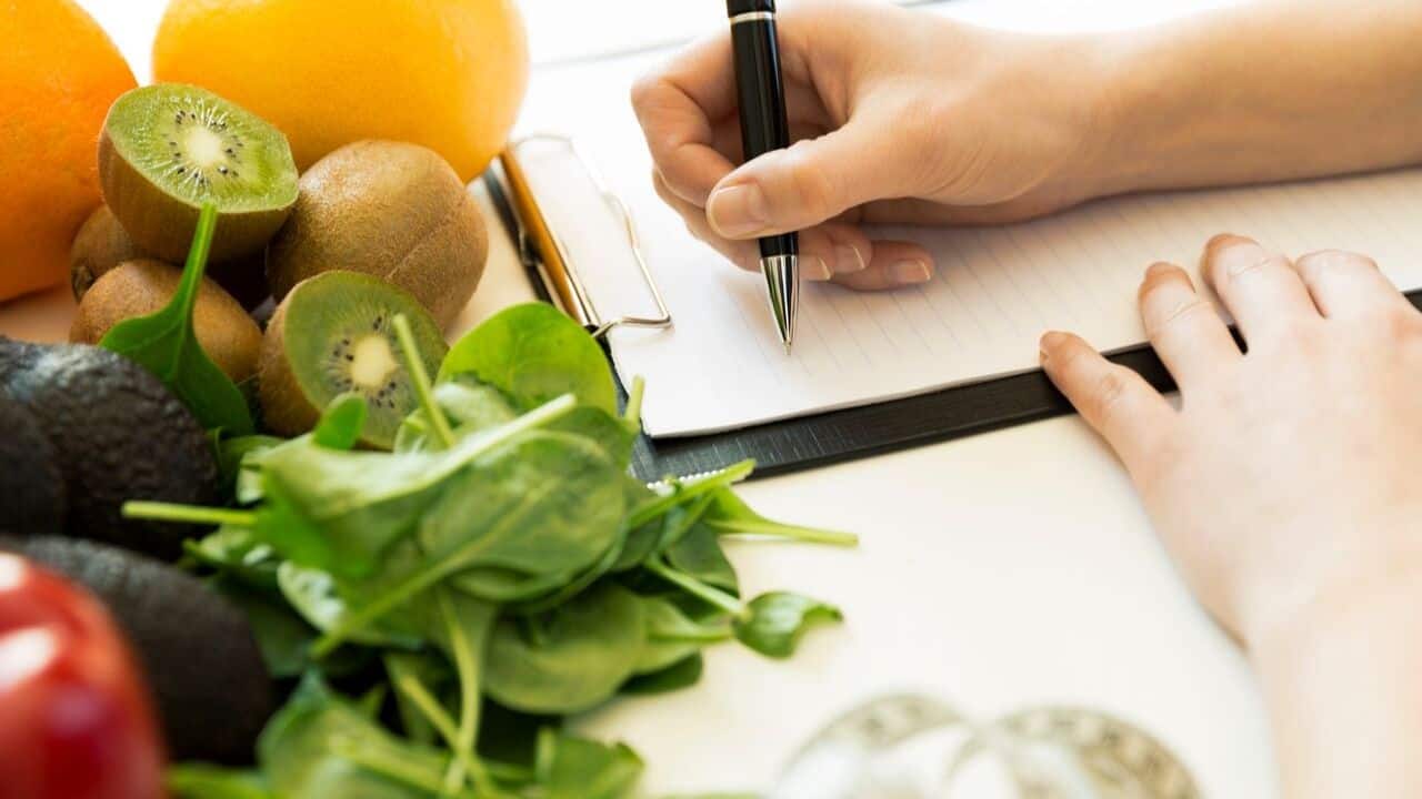 Fruits and vegetables with a woman’s hand writing in a notebook