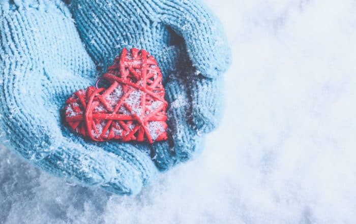 Woman wearing blue gloves holding a red heart-shaped Christmas ornament