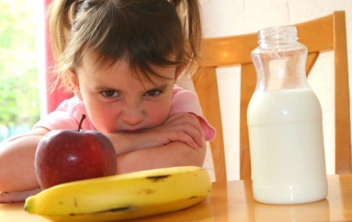 Young girl showing frustration, not wanting to eat fruit or drink milk