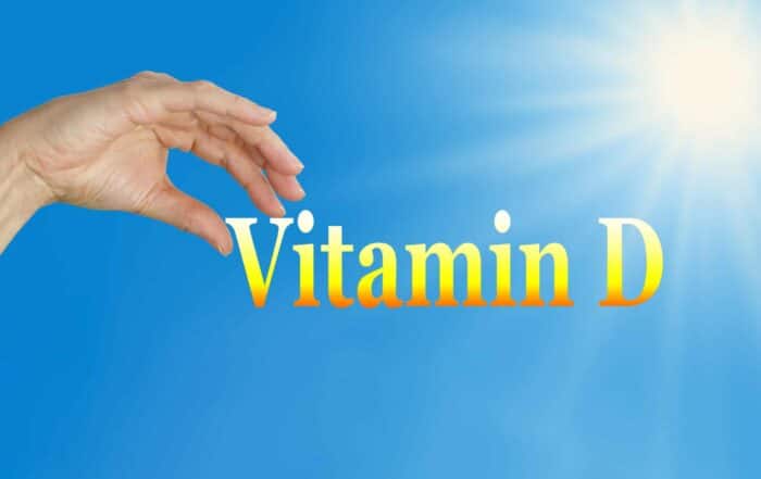 Sunshine and blue sky background with the word Vitamin D and a female hand poised to pick the D with plenty of copy space below